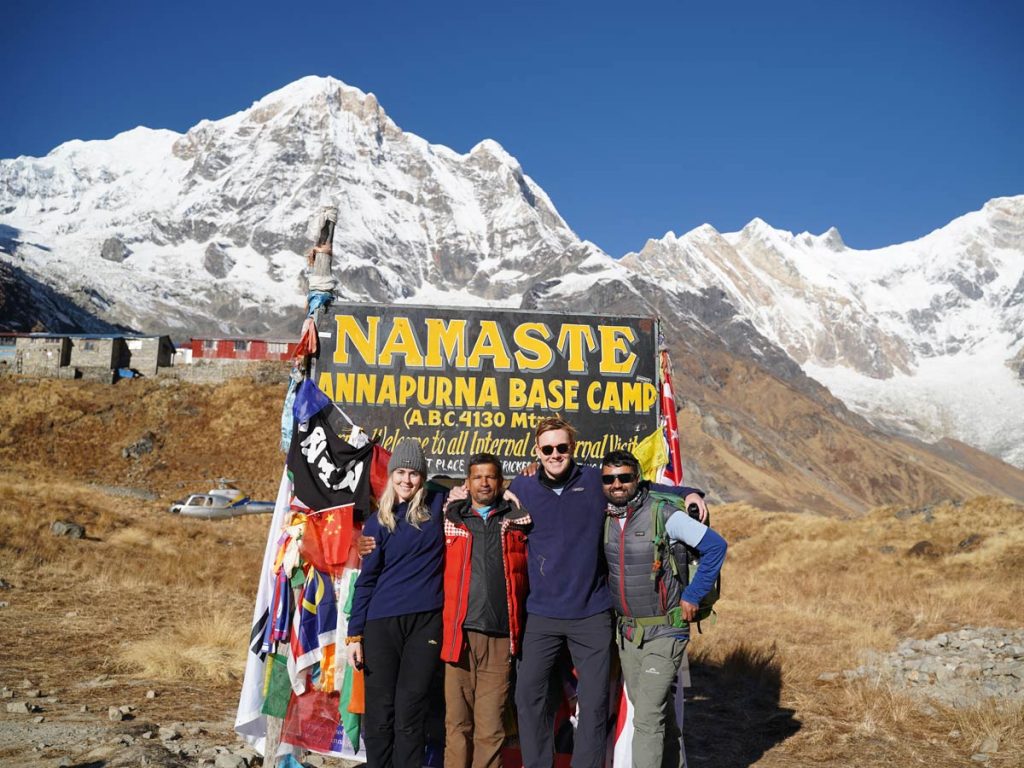 Group of joyful trekkers celebrating at Annapurna Base Camp, surrounded by breathtaking mountain scenery.